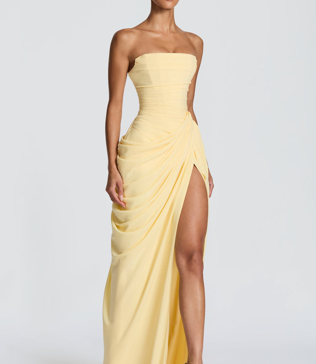 Three-quarter view pale yellow strapless corset maxi womens dress showing draped skirt and thigh split