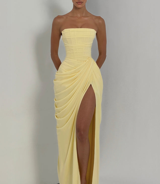 Lifestyle shot pale yellow strapless corset maxi womens dress with draped skirt and high slit