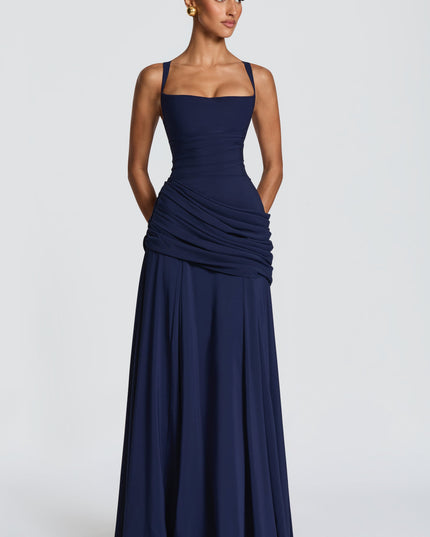 Full length navy blue square neck maxi dress with draped overlay and flared skirt, angled pose