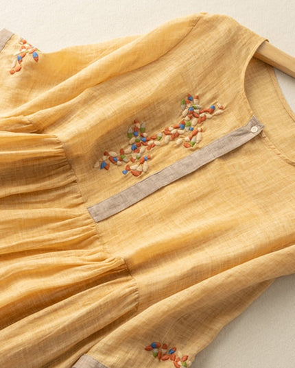 Close-up of mustard yellow embroidered midi dress showing floral chest detail and sleeve trim
