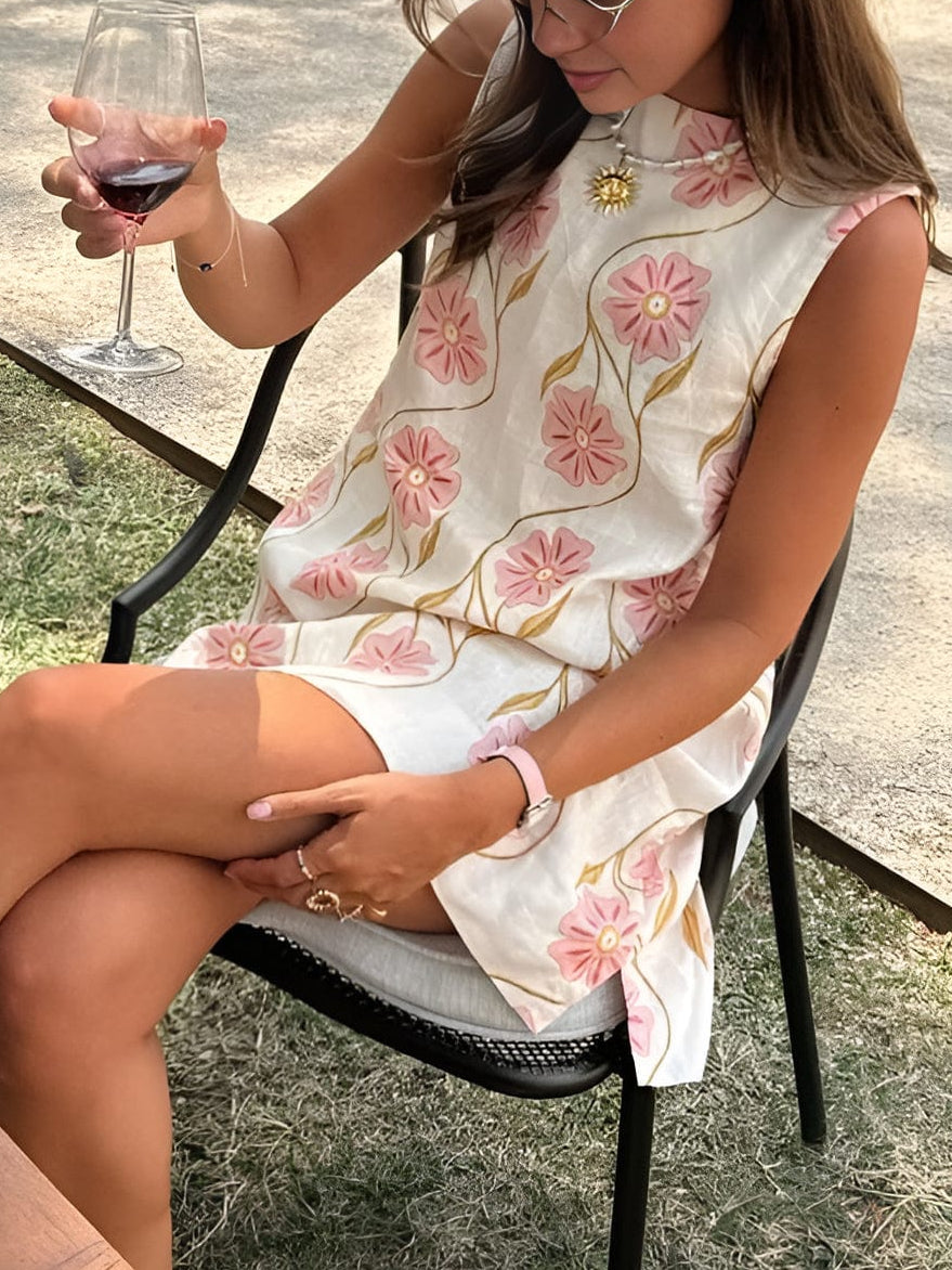 Women's summer floral sleeveless mini dress shown seated, with pink blossoms and a relaxed loose fit