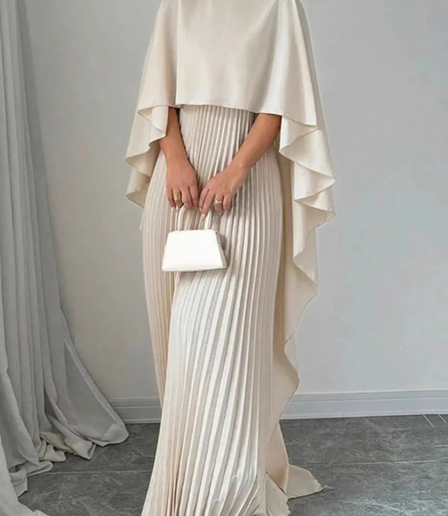 Front view of cream formal maxi dress with cape overlay, pleated skirt, and clutch