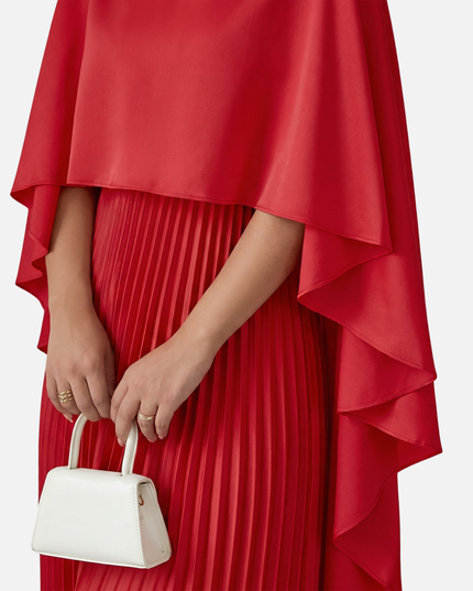 Close-up of red formal maxi dress with cape overlay and vertical pleats on the skirt