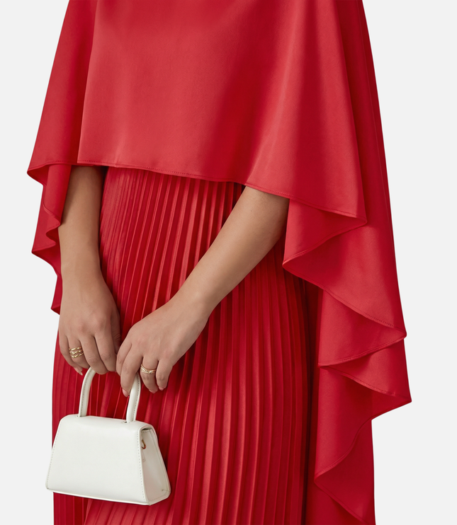 Close-up of red formal maxi dress with cape overlay and vertical pleats on the skirt
