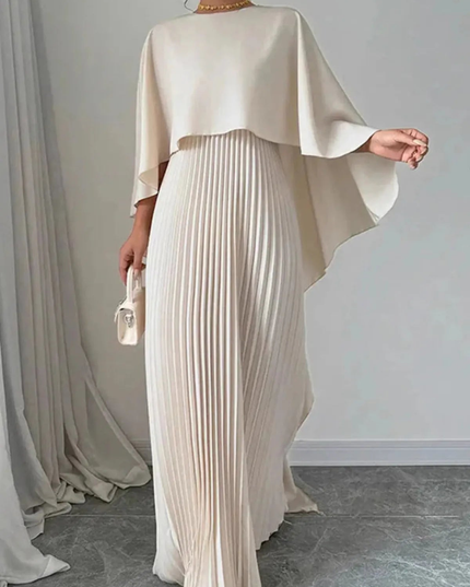 Full-length cream women's formal maxi dress with cape overlay and pleated skirt indoors