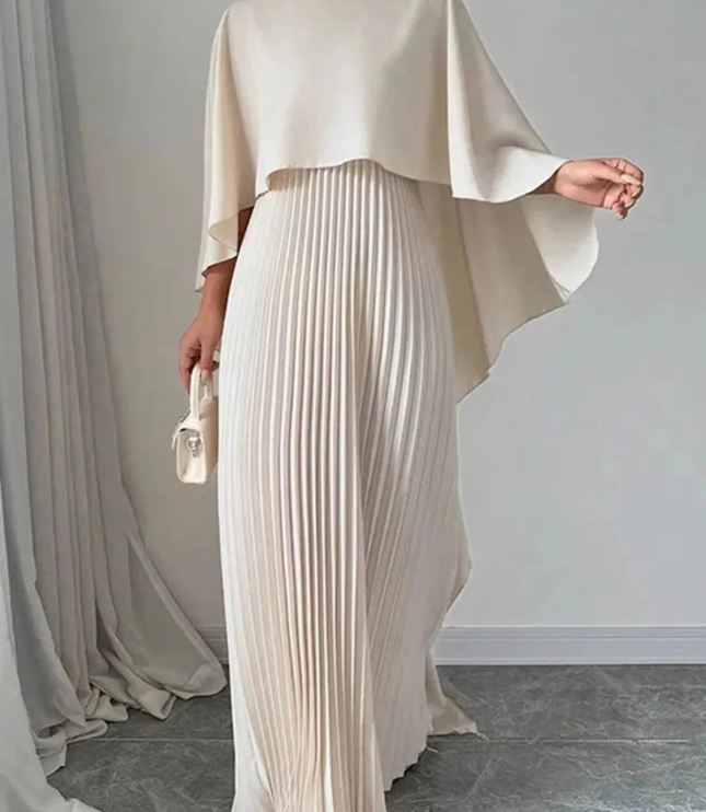 Full-length cream women's formal maxi dress with cape overlay and pleated skirt indoors