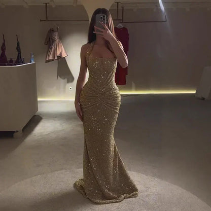 Gold sequin halter maxi dress full length in low light, ruched waist and flared hem