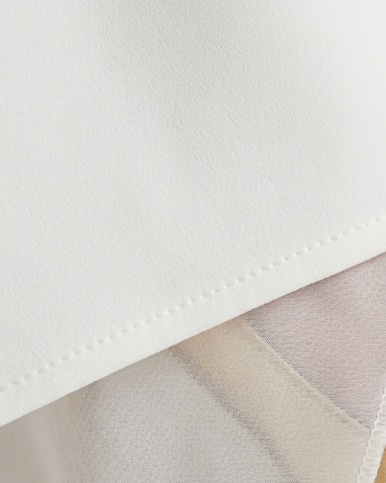 Close-up of white asymmetric maxi dress fabric with clean hem and slit detail