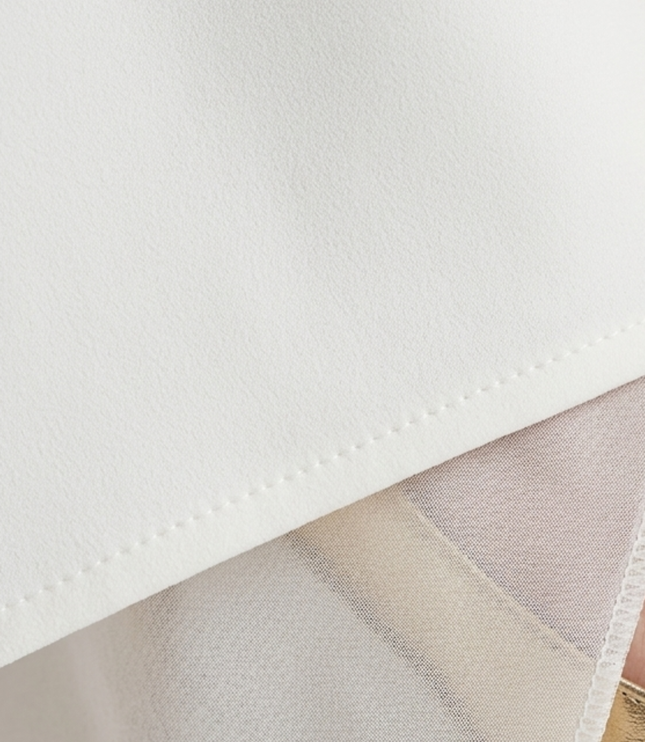 Close-up of white asymmetric maxi dress fabric with clean hem and slit detail