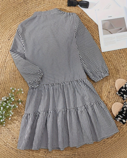 Black and white gingham mini dress laid flat, showing long sleeves and tiered hem