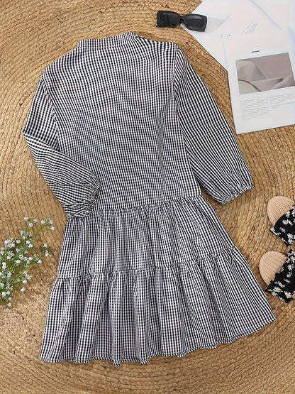 Black and white gingham mini dress laid flat, showing long sleeves and tiered hem