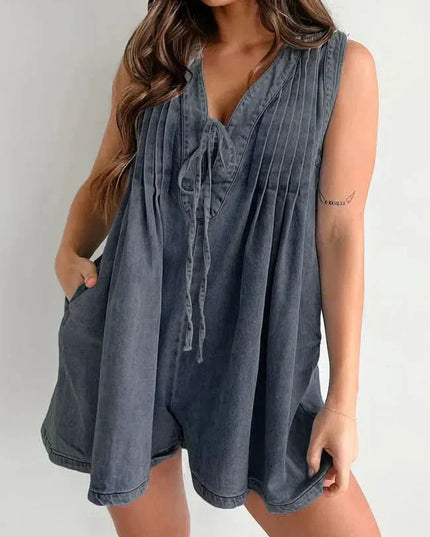 Dark washed mini denim romper for women with V-neck tie front, pleated bodice, and relaxed shorts