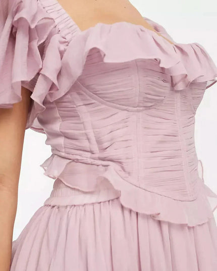 Back view of blush pink wedding guest dress with open back, ruffled sleeves, and full midi skirt
