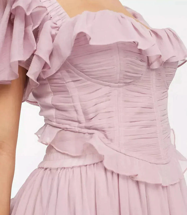 Back view of blush pink wedding guest dress with open back, ruffled sleeves, and full midi skirt