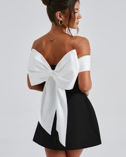 Back angled view of black off shoulder mini dress with large white bow and open back detail