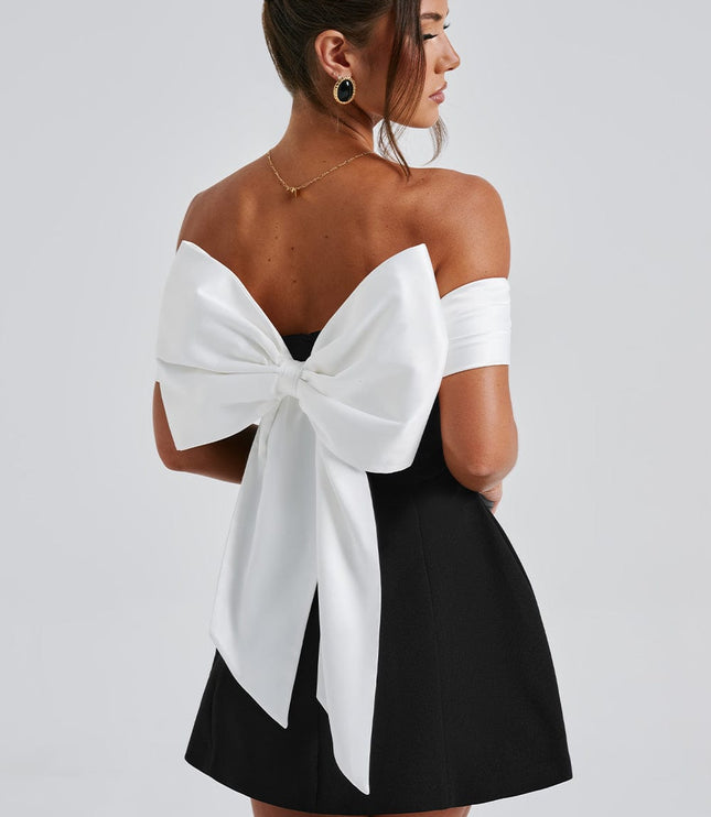 Back angled view of black off shoulder mini dress with large white bow and open back detail