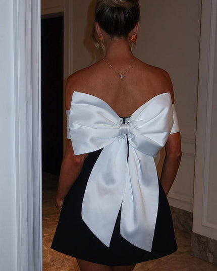 Back view of black mini dress with white bow tie detail, off shoulder sleeves, and flared skirt