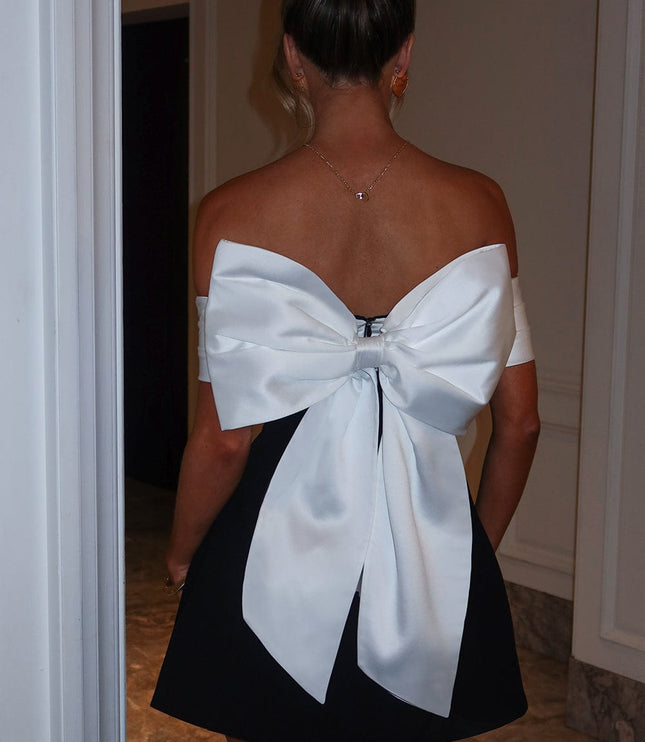 Back view of black mini dress with white bow tie detail, off shoulder sleeves, and flared skirt