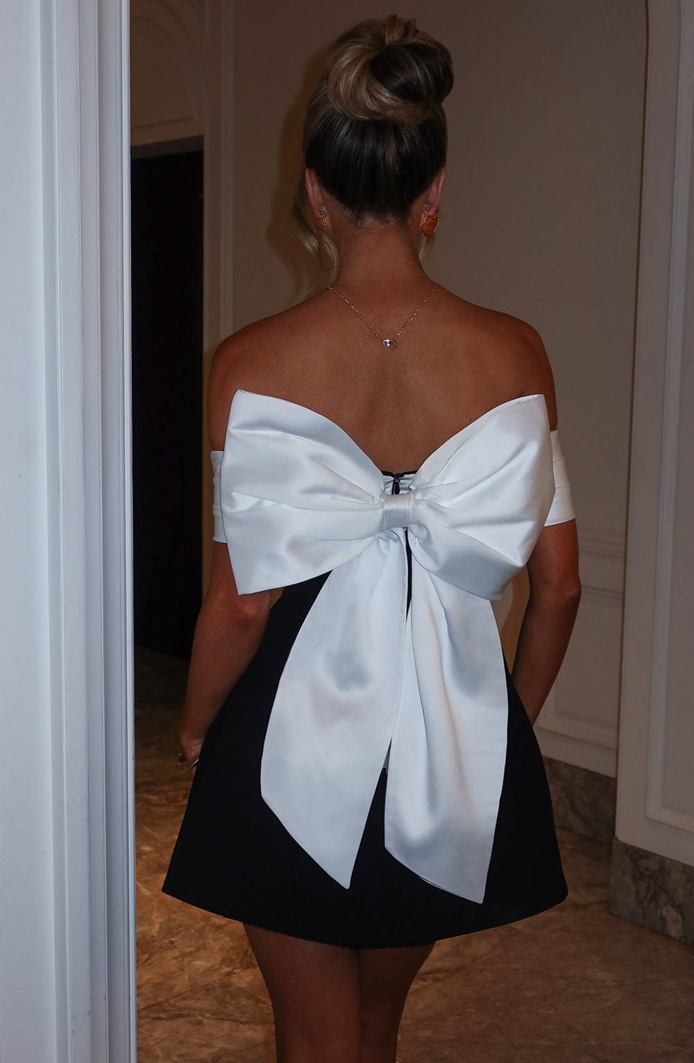 Back view of black mini dress with white bow tie detail, off shoulder sleeves, and flared skirt
