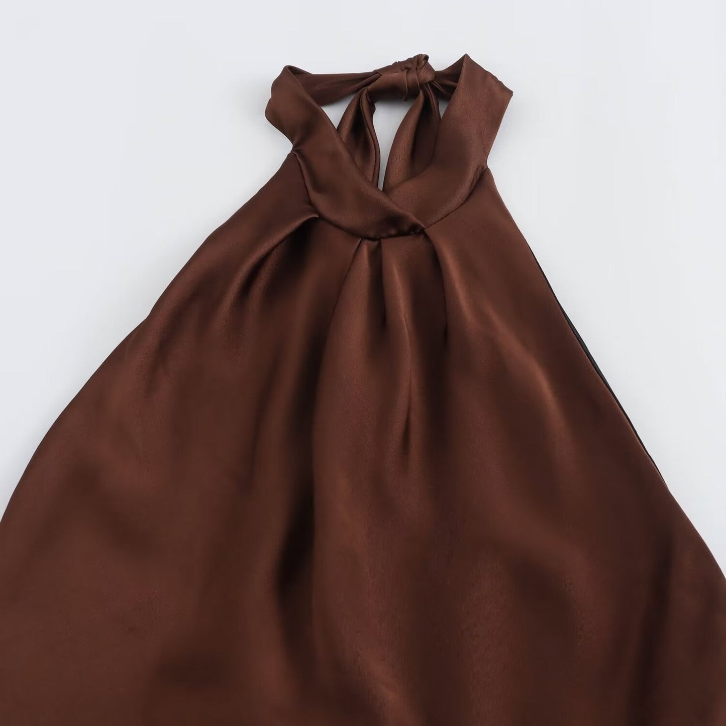 Flat lay of brown satin halter midi dress showing tied halter neckline and flowing skirt