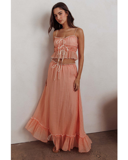 Peach summer maxi skirt set with ruched crop top, long skirt, and ruffled hem against wall