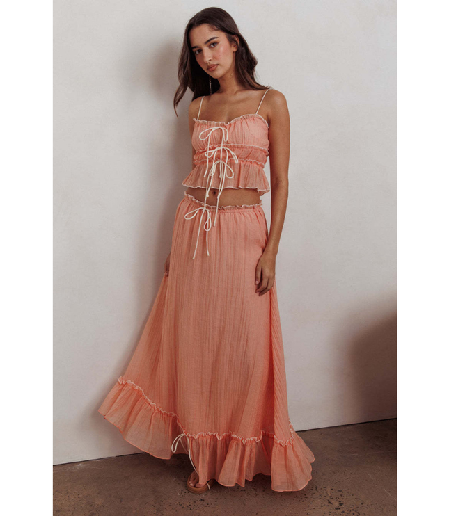 Peach summer maxi skirt set with ruched crop top, long skirt, and ruffled hem against wall