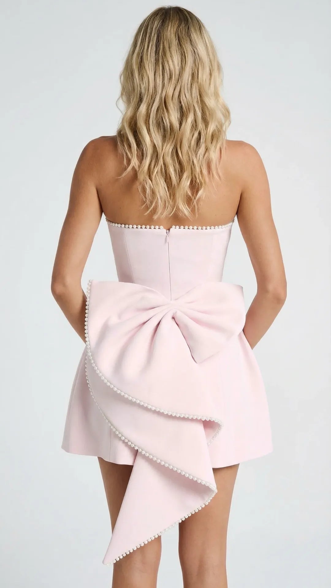 Back view of pink strapless dress with pearl trim and large bow detail