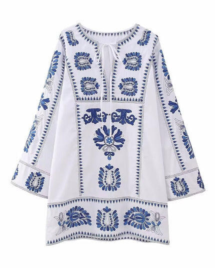 Front view of white embroidered mini dress with tie neckline, blue floral accents, and bell sleeves