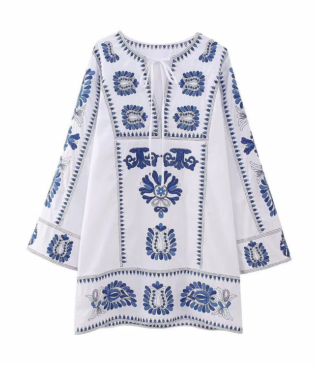 Front view of white embroidered mini dress with tie neckline, blue floral accents, and bell sleeves