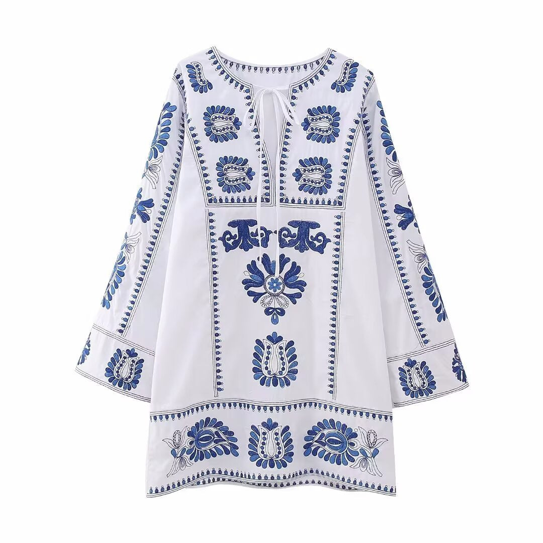 Front view of white embroidered mini dress with tie neckline, blue floral accents, and bell sleeves