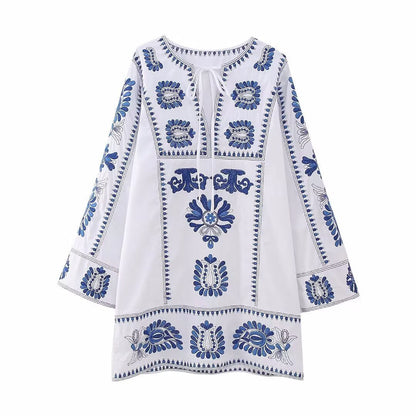 Front view of white embroidered mini dress with tie neckline, blue floral accents, and bell sleeves