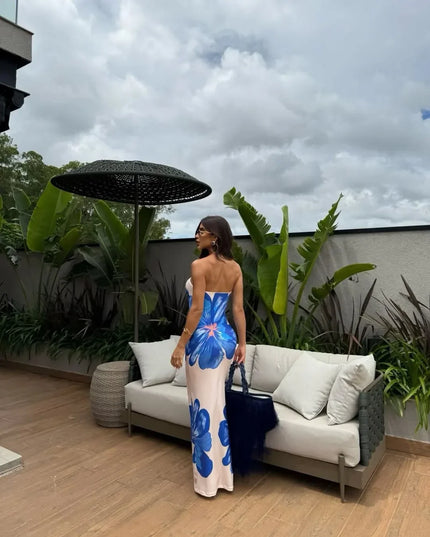 Front view of cream floral strapless maxi dress with orange flower print by a pool