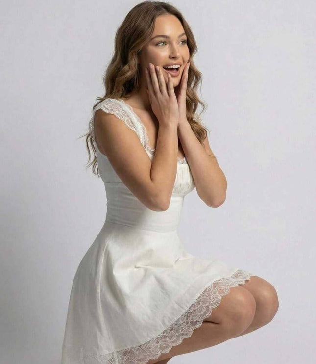 White lace mini dress with square neckline and scalloped hem, worn in a seated pose