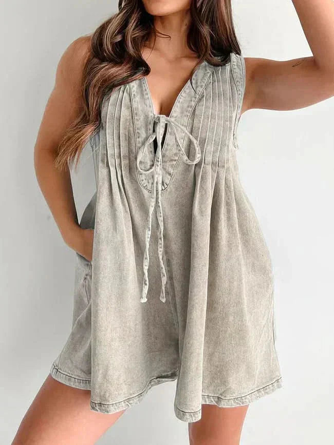 Beige washed casual mini denim romper with pleated front, tie neckline, and sleeveless summer style