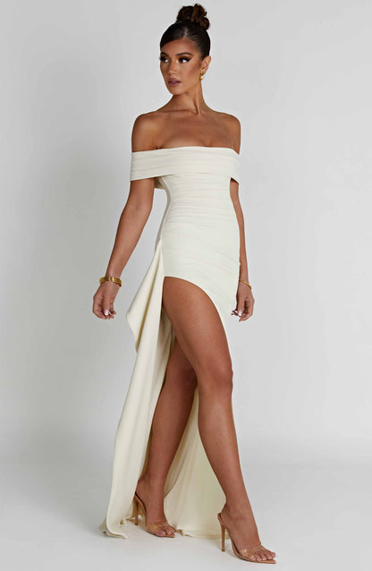 Side view of cream formal maxi dress with off shoulder neckline and draped back panel
