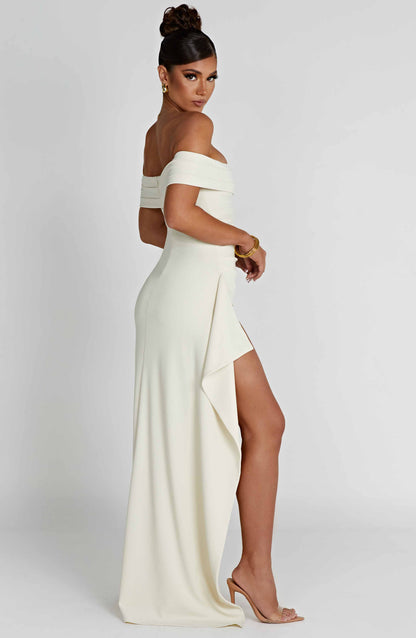 Back side view of cream off shoulder maxi dress with long flowing skirt and slit