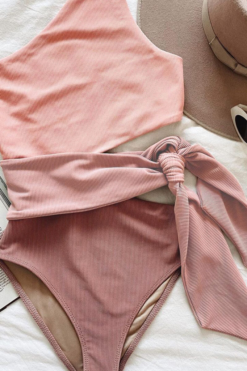Folded pink ribbed one piece swimsuit with one shoulder cutout and matching waist tie