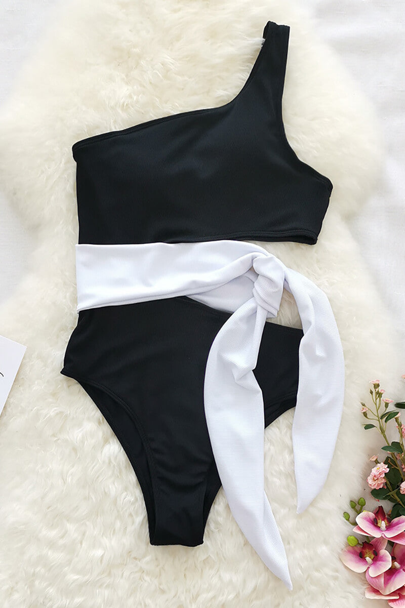 Flat lay of black one shoulder one piece swimsuit with white waist tie and cutout