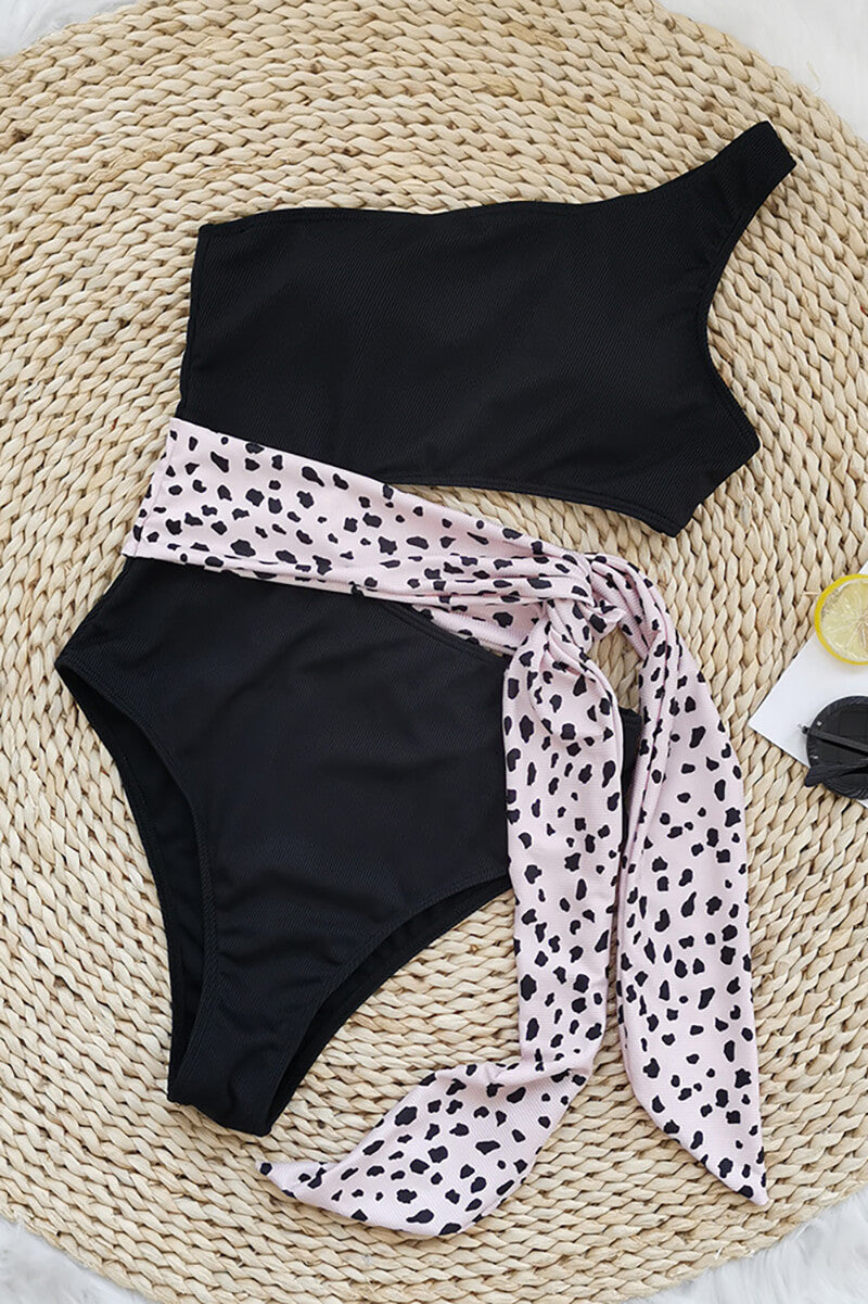 Black one shoulder one piece swimsuit with pink leopard print waist tie in flat lay
