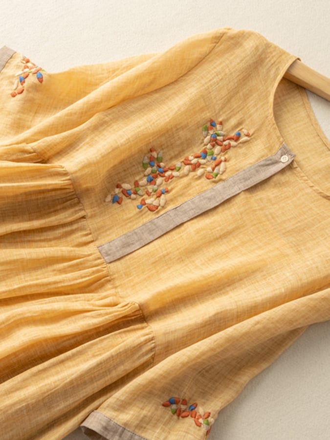 Close-up of mustard yellow embroidered midi dress showing floral chest detail and sleeve trim