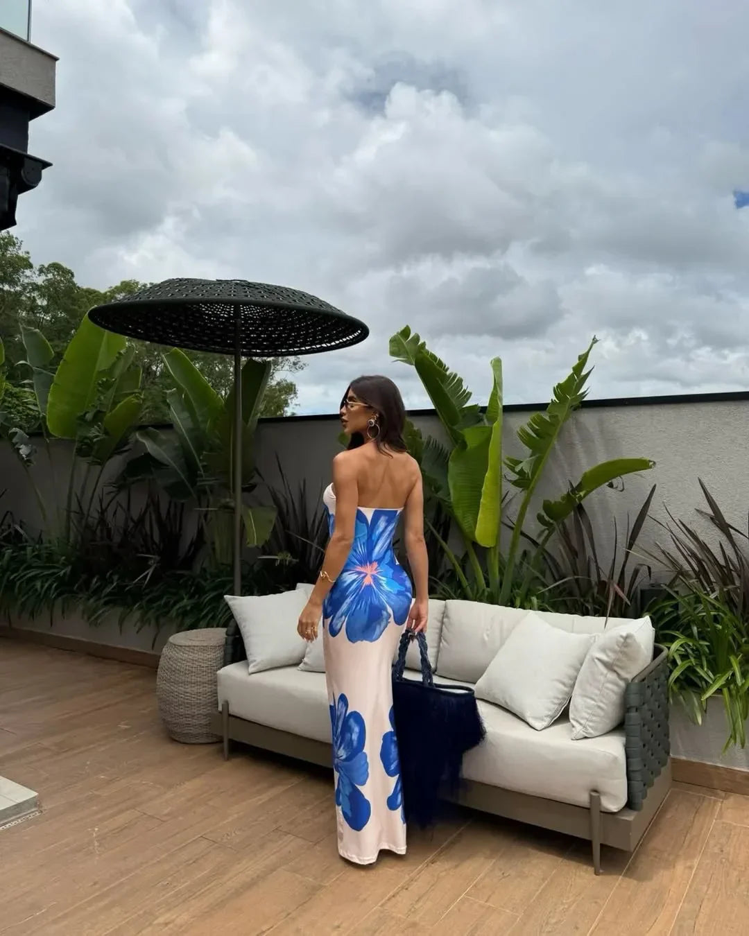 Front view of cream floral strapless maxi dress with orange flower print by a pool