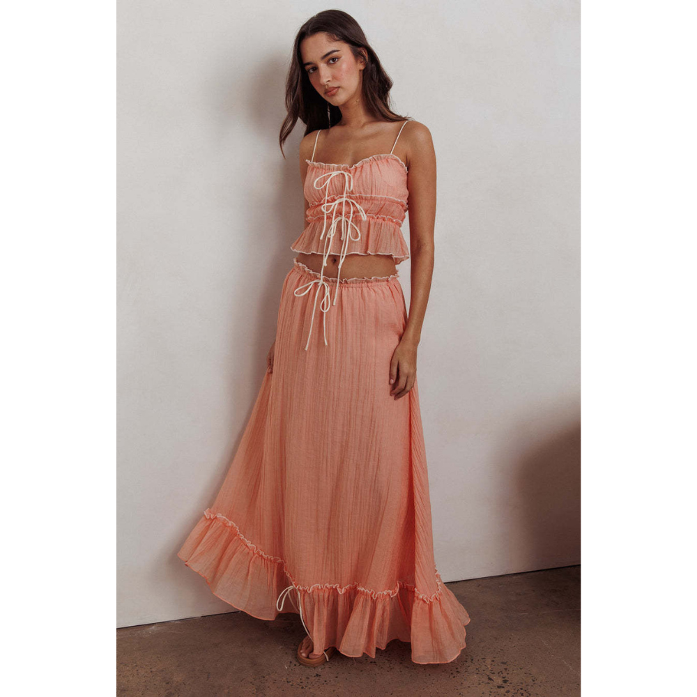 Peach summer maxi skirt set with ruched crop top, long skirt, and ruffled hem against wall