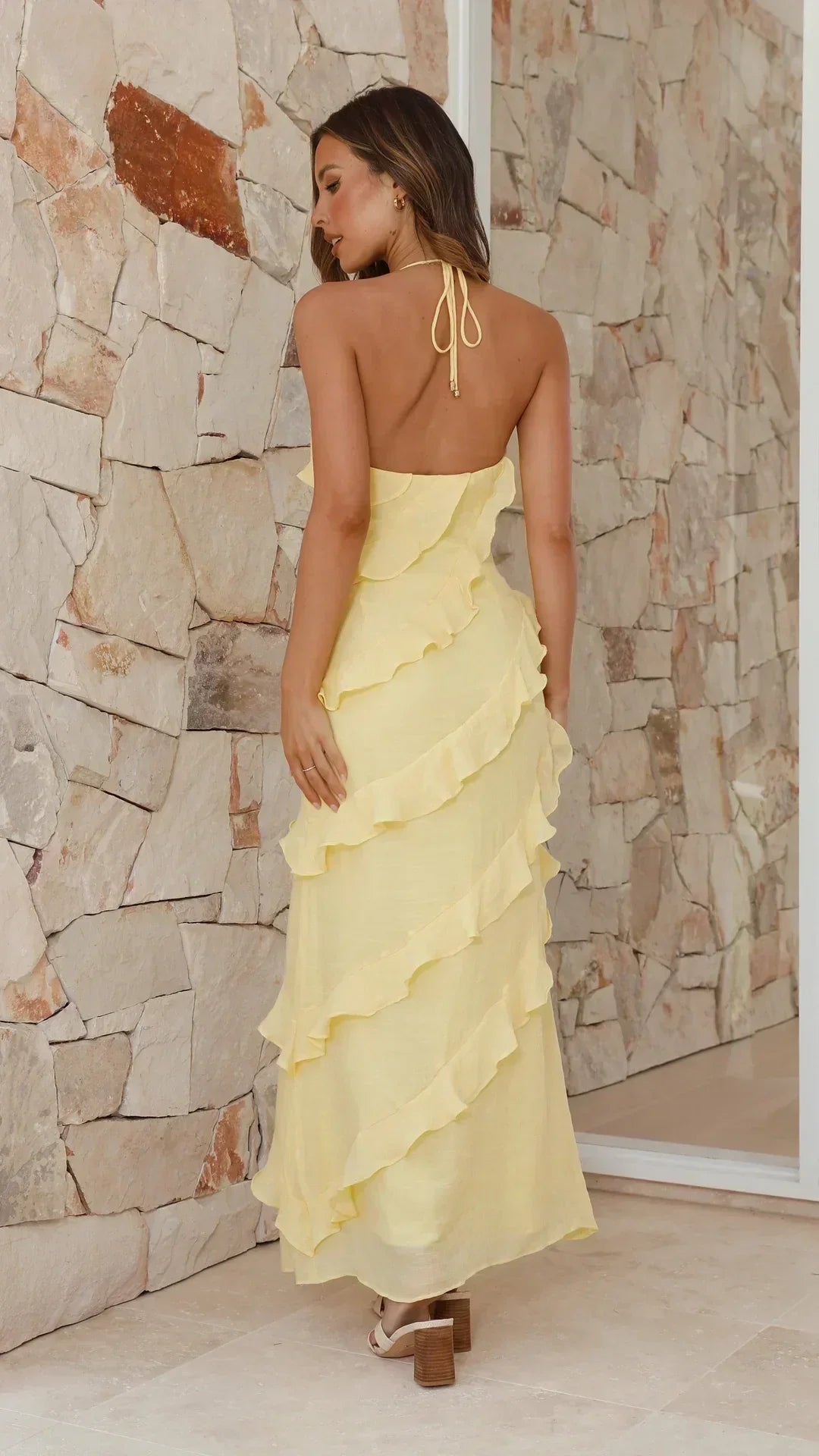 Back view of pale yellow maxi dress with open back and ruffle layers, styled with heeled sandals