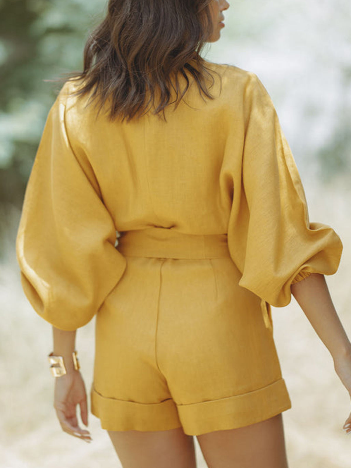 Back view of mustard yellow long sleeve collared romper with waist tie and cuffed shorts