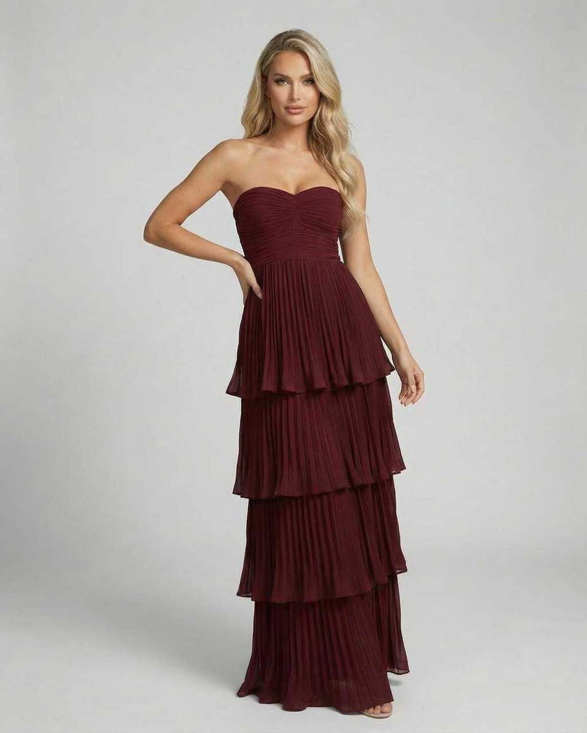 Front view of burgundy strapless wedding guest maxi dress with layered pleated skirt